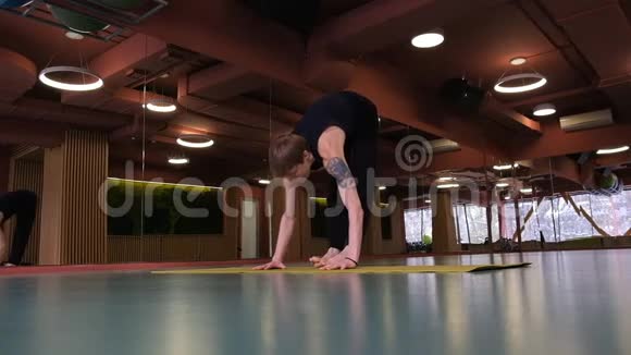 一个有纹身的年轻人正在健身房做瑜伽他站在双手上抬起双腿广角视频的预览图