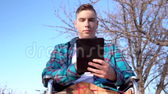 坐轮椅的年轻人拿着平板电脑自然界中的残疾人在平板电脑上通信视频的预览图