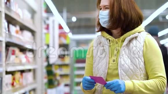 戴着医用口罩和手套的女孩在超市里看购物清单视频的预览图