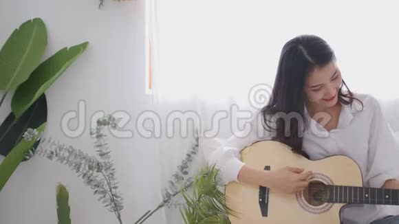 美丽的亚洲女人在卧室里玩吉他带着快乐的情绪视频的预览图