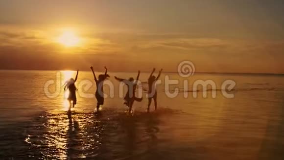 一群快乐的女孩在海滩上奔跑玩耍在夕阳下跳舞在夏天的夕阳下喷洒海滩视频的预览图