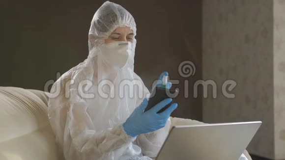 一个自我孤立的女人坐在家里的沙发上穿着防护服和防护面罩给她消毒视频的预览图