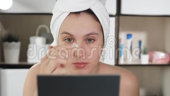 面霜浴室里的女孩用毛巾和镜子轻轻地把奶油涂在脸上涂抹到吸收为止视频的预览图