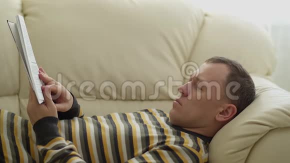 阳光明媚的一天男人躺在沙发上看书视频的预览图