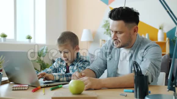小孩在爸爸和他说话的时候用手提电脑在家里用书桌教他视频的预览图