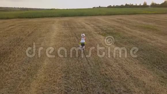 一个穿着白色连衣裙的女人带着向日葵在田野上骑自行车的俯视图视频的预览图