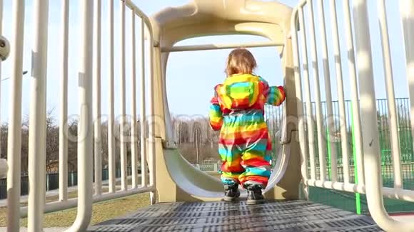 一个穿着彩色彩虹衣服的孩子从操场上的滑梯上骑着春天游乐散步和乐趣幼儿视频的预览图
