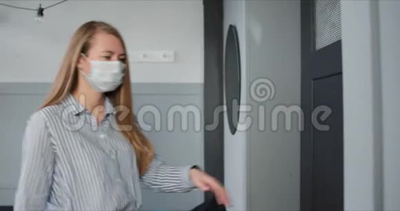 年轻的高加索女人戴着医疗面具打开公寓门在病毒检疫期间从快递员那里得到包裹视频的预览图