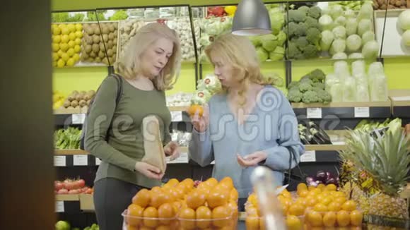 两个成年白种人家庭主妇在杂货店采摘橘子严肃的高级妇女把水果放进纸袋里视频的预览图