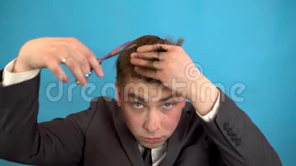 商人把自己的头发剪在蓝色的背景上一个穿西装的人用剪刀修剪自己视频的预览图