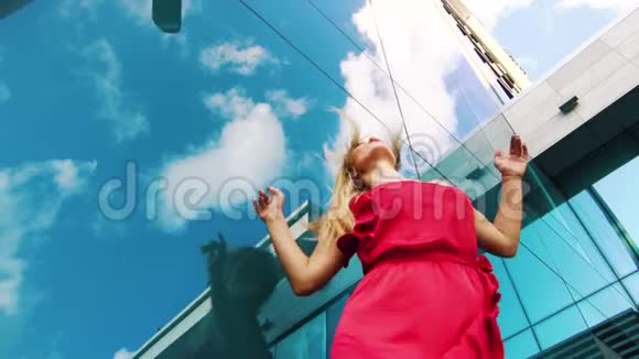一位穿着红色连衣裙的可爱女子在摩天大楼的玻璃墙附近跳舞视频的预览图