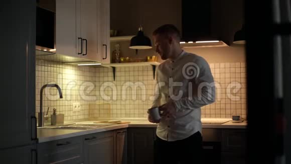 英俊的胡子男人在现代黑暗的厨房里用自来水填充玻璃然后喝它视频的预览图