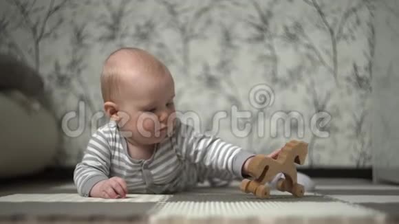一个穿着条纹睡衣的金发小宝宝和一匹木马在地板上玩耍试图吃掉它视频的预览图