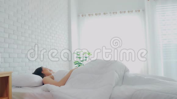 女人在床上醒来后伸展手臂看着外面的窗户视频的预览图