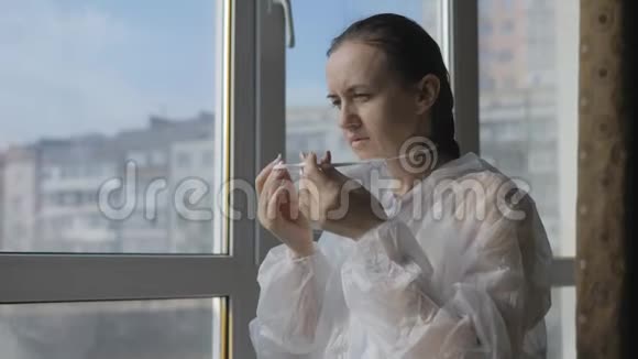 在大流行病毒时期一名妇女穿着防护服戴着面具站在窗边视频的预览图