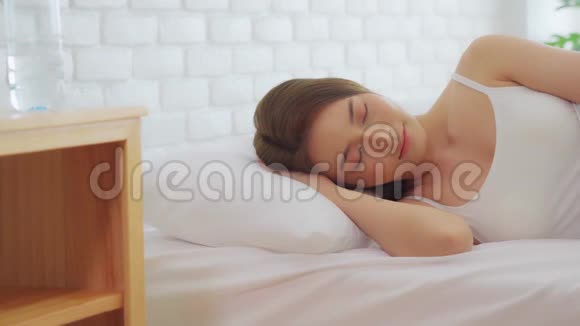 美丽迷人的亚洲女人穿着睡衣睡觉闭上眼睛微笑着睡觉在卧室的床上做着甜蜜的梦视频的预览图