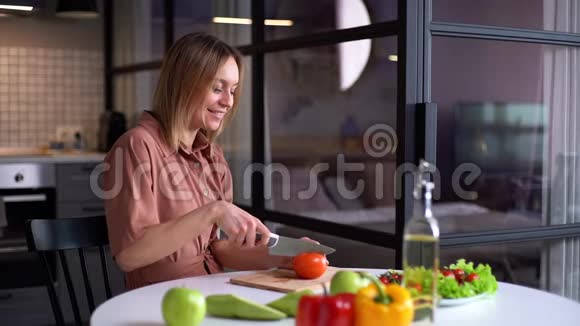 快乐的年轻女人用刀子切新鲜的有机番茄做蔬菜沙拉视频的预览图
