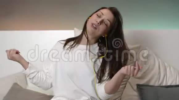 一个英俊的女孩带着黄色耳机在家里的床上听音乐笑着视频的预览图