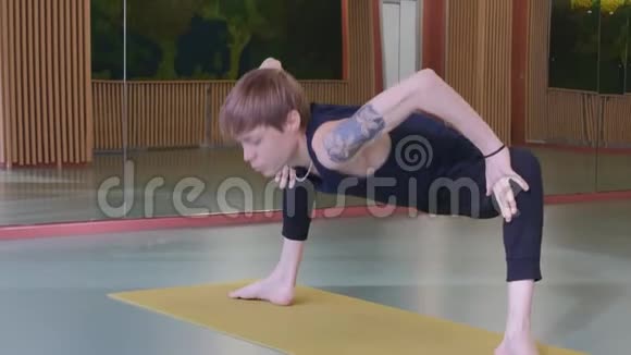 一个年轻可爱的家伙做瑜伽体式他在一个房间里学习房间里有黄色地毯上的镜子他的动作很流畅而且视频的预览图