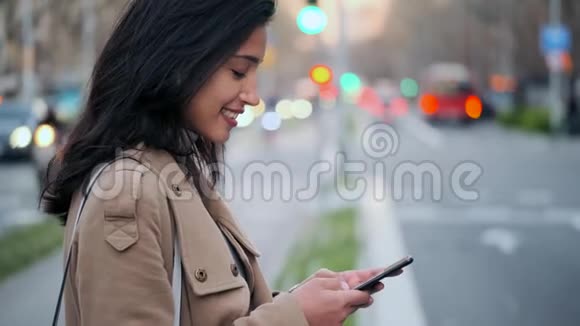 漂亮的年轻女人在路边等着在手机上发短信视频的预览图