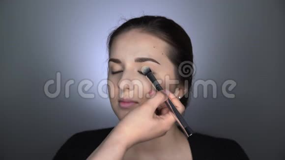 为坐在工作室的美丽而华丽的女人化妆的过程化妆师用粉末视频的预览图