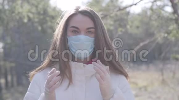 白种人年轻女子戴着面具打喷嚏的肖像布鲁内特冠状病毒携带者站在阳光明媚的春天公园视频的预览图