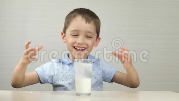 一个快乐的笑着的男孩坐在桌子旁喝牛奶或酸奶健康有机食品各种情绪视频的预览图