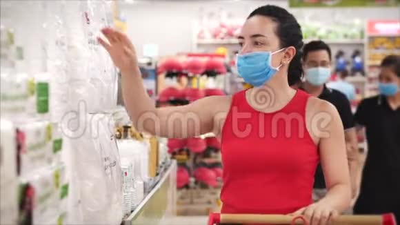 戴着冠状病毒流行口罩的年轻女性在超市购物选择卫生纸人们在一个视频的预览图