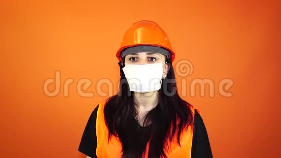 女建筑工人穿着工作服和医用口罩在橙色背景下咳嗽感染威胁的概念视频的预览图