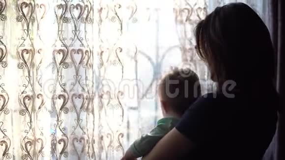 一位年轻的母亲抱着一个婴儿一个女人带着一个孩子看着窗外推着窗帘视频的预览图