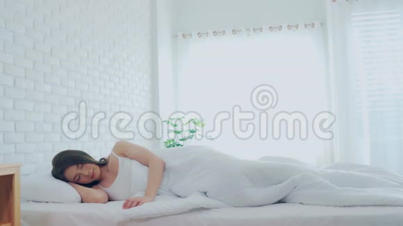 女人在床上醒来后伸展手臂看着外面的窗户视频的预览图