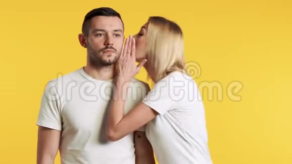 年轻女子在黄色背景下向惊讶的男人低语秘密视频的预览图