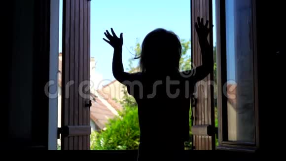 一个快乐的小女孩在窗户的背景上挥舞着双手的剪影视频的预览图
