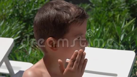 一个晒黑的小男孩正在用防晒霜涂抹他的脸颊视频的预览图