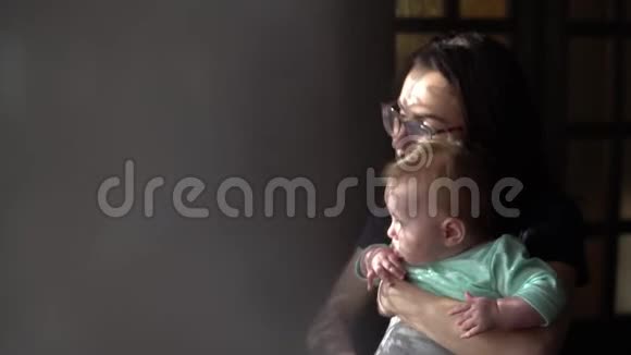 一位年轻的母亲抱着一个婴儿一个带着孩子的女人看着窗外视频的预览图