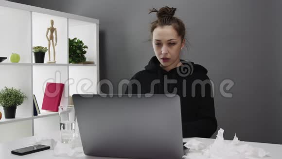 一个漂亮的女孩在家里用笔记本电脑做隔离工作还经常打喷嚏视频的预览图