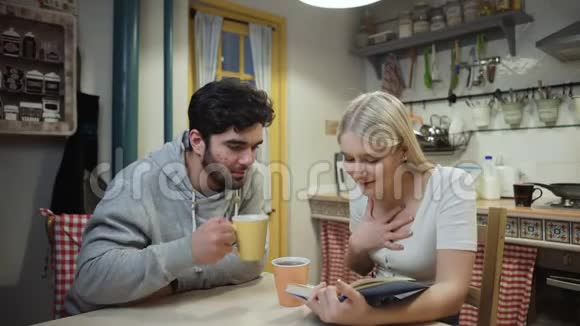 年轻夫妇喝茶讨论一本关于厨房的书视频的预览图