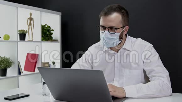 戴防护面具的英俊商人在隔离电脑上远程工作视频的预览图
