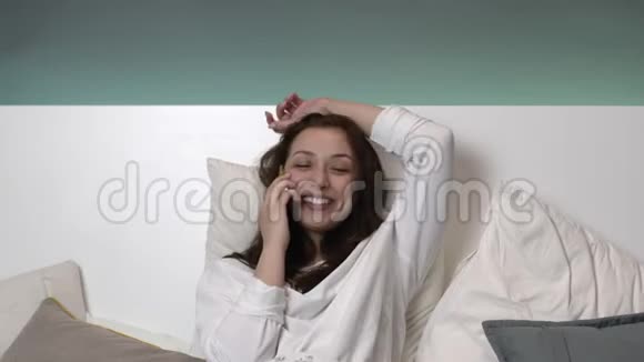 穿着白色睡衣的快乐性感棕色头发女孩睡前交流视频的预览图