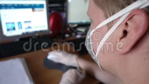 戴防护面罩和手套的年轻人因冠状病毒检疫而在家用电脑工作视频的预览图