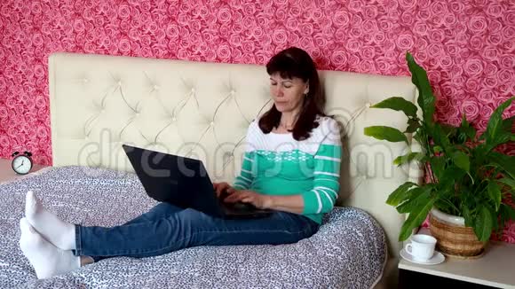从家里远程工作一位成年白人妇女正在床上卧室里的笔记本电脑上工作e的概念视频的预览图