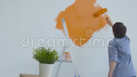 平面改造概念快乐的中年妇女用油漆滚筒画白色的墙橙色的油漆视频的预览图