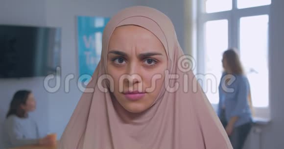 一位年轻美丽严肃愤怒的穆斯林女孩在头巾办公室背景下的特写肖像视频的预览图