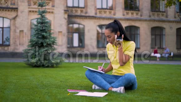 聪明的女学生坐在公园的草地上听一个声音信息4K视频的预览图