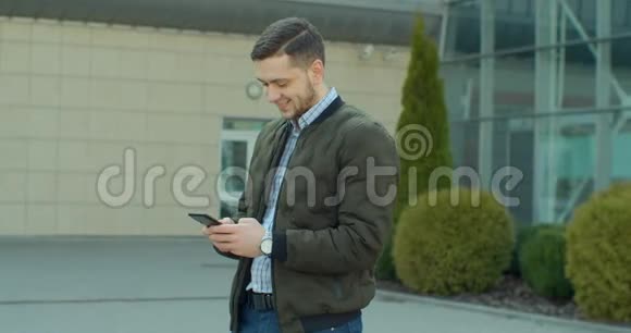 城市街道上的年轻人使用手机打字和朋友聊天男人在户外使用手机视频的预览图