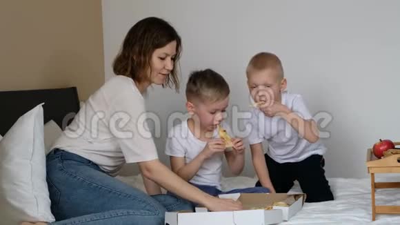 带着孩子在床上吃披萨的家庭母亲微笑着视频的预览图