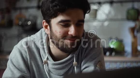 一个快乐的男人晚上在厨房里用笔记本电脑工作视频的预览图