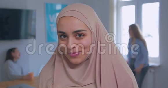 一位年轻美丽谦虚的穆斯林女孩在头巾办公室背景下的特写肖像视频的预览图