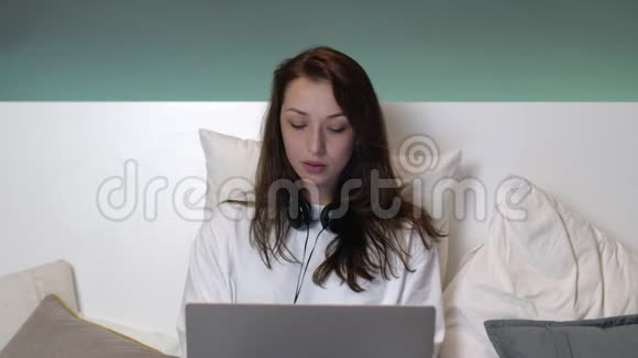 漂亮的白种人女人穿着睡衣在床上长头发在笔记本电脑上工作视频的预览图