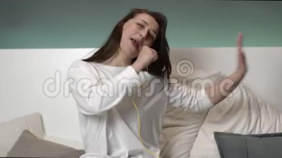 快乐的女人带着黄色耳机在家里的床上听音乐微笑着视频的预览图